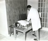 <div class=lightGallery-captions><p>Centro Sanitario de Rehabilitación de Mutua de Ceuta</p><p>Detalle de camilla con paciente y rehabilitador en centro de Prevención y Rehabilitación</p><h4>Material cedido por 115 - CESMA</h4><span>1934</span></div>